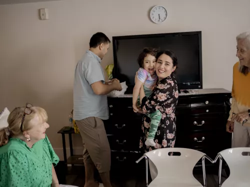 Surrounded by two blonde women and a man, a happy young woman smiles as she holds her disabled child in her arms 