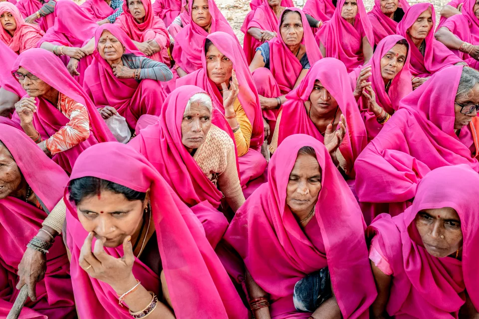 Close view of seated women in pink saris, with serious, attentive expressions.