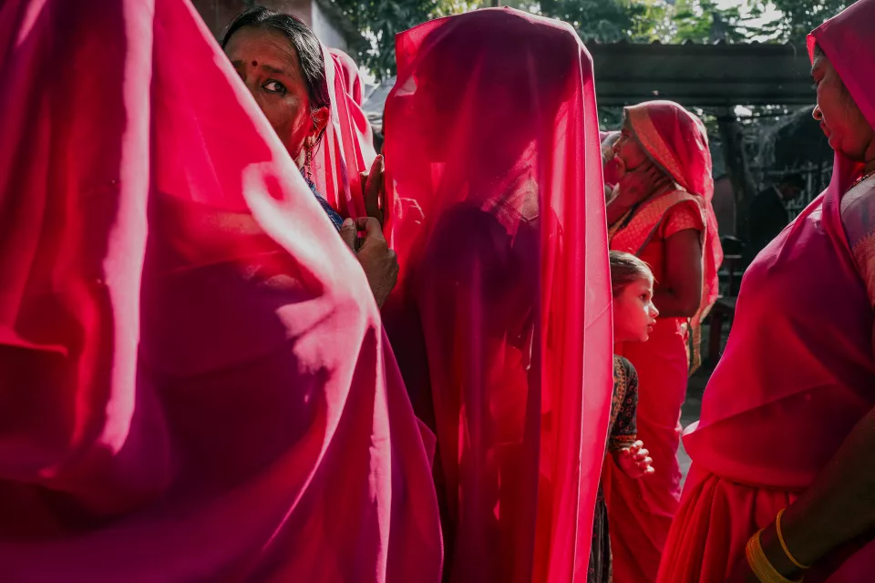 Close-up of women in pink saris with serious faces, a young girl leaning against one of them.