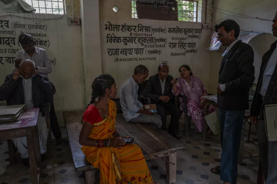 People sit and talk in a small legal office with Hindi names of lawyers painted on the wall.