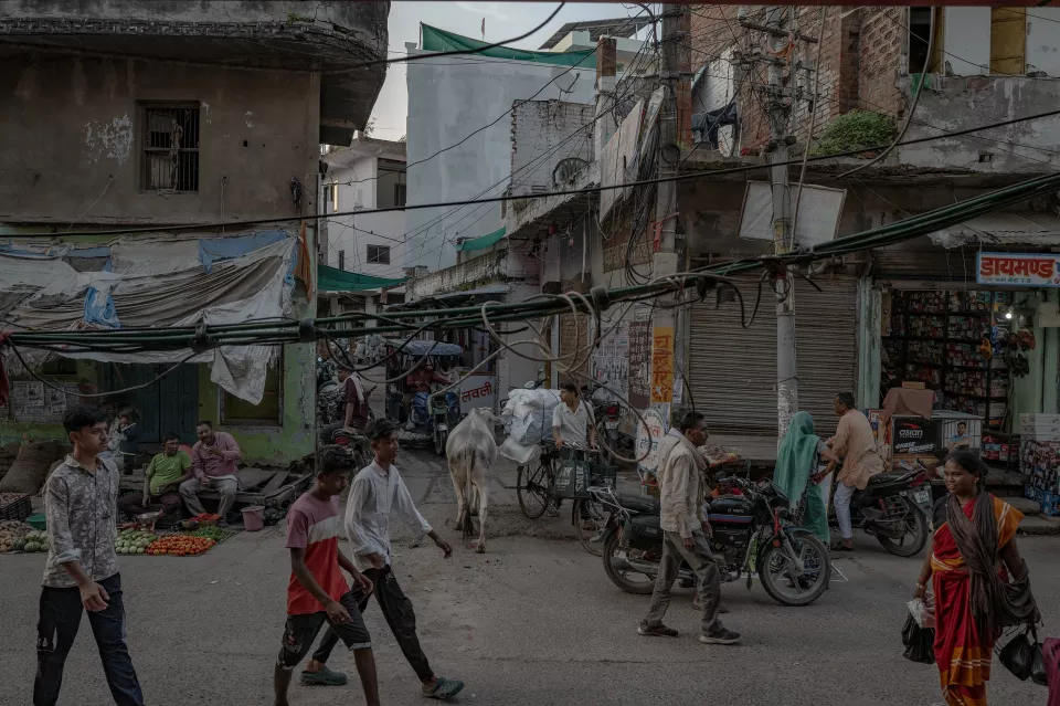People, a cow and motorbikes crowd a busy market street tangled with overhead wires.