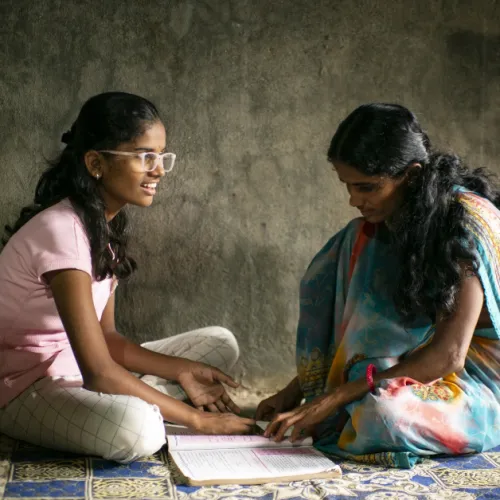 Two women sit on the floor with an open notebook
