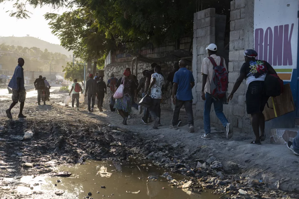 People walking along elevated path next to standing water and debris