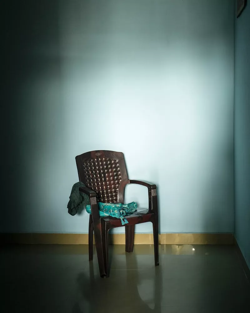 Empty plastic chair against a teal-blue wall in a sparsely furnished room