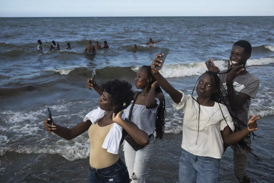 Four young people standing in shallow ocean waves taking selfies with phones