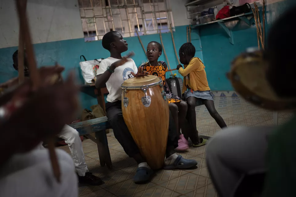 Indoor capoeira session with youth gathered around a large wooden drum 