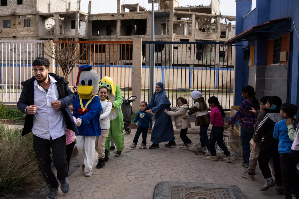 Children in single file laugh behind a volunteer dressed as Donald Duck and Dr. Khaldoun Muawiyah Al-Mallah, who leads the line.