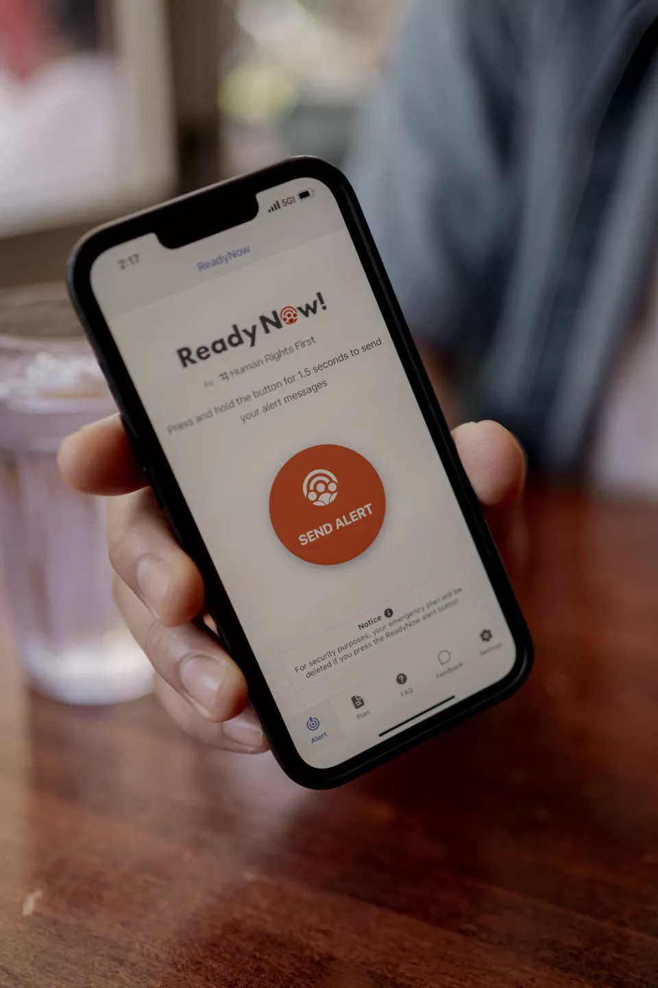 A hand shows a cell phone screen. It displays a button to press to alert others to the presence of ICE.